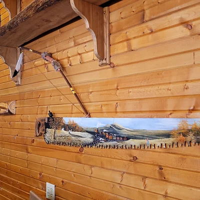 Hand-painted mountain scene on a saw blade above the log wall