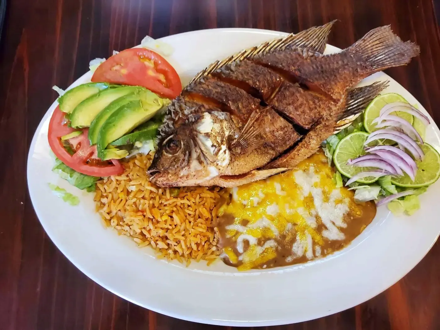 Whole fried tilapia with rice, beans, and avocado